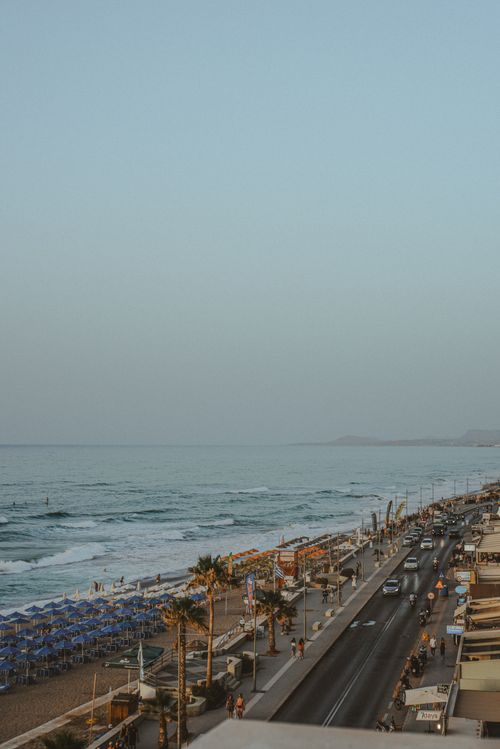 Free Stunning aerial view of a coastal road lined with palm trees and beachfront umbrellas at sunset. Stock Photo