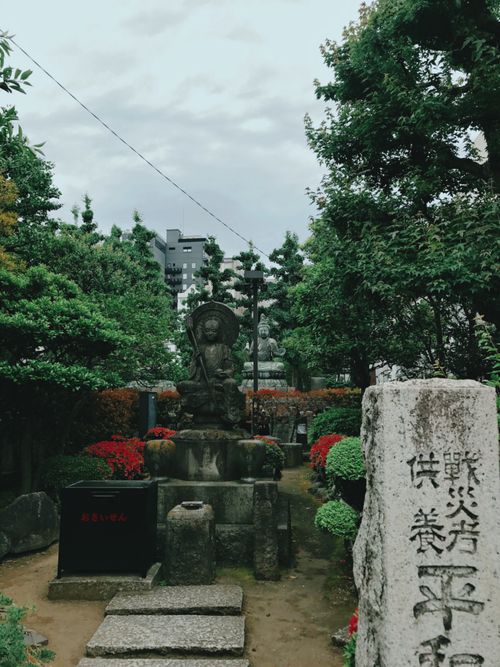 Free Serene Buddhist statue surrounded by lush greenery in Taito City, Tokyo, under cloudy skies. Stock Photo