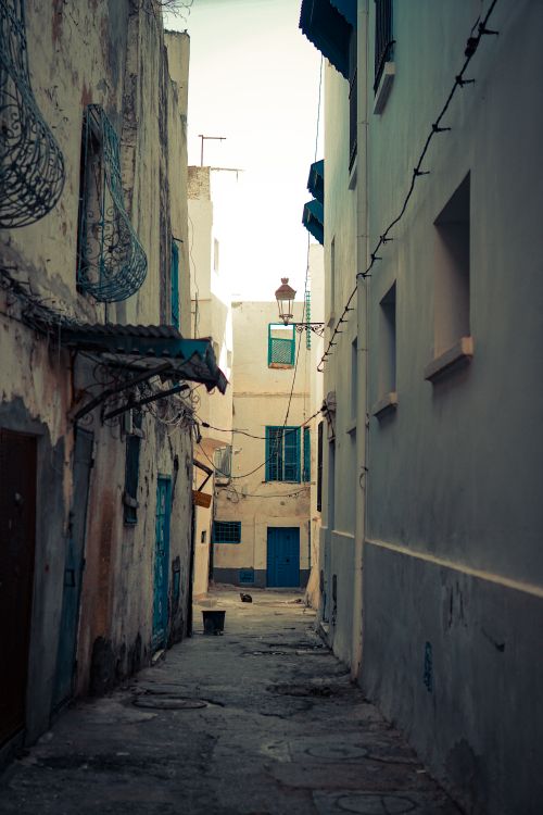 Free A narrow alley with rustic charm in a Mediterranean village, featuring weathered buildings and vibrant blue accents. Stock Photo