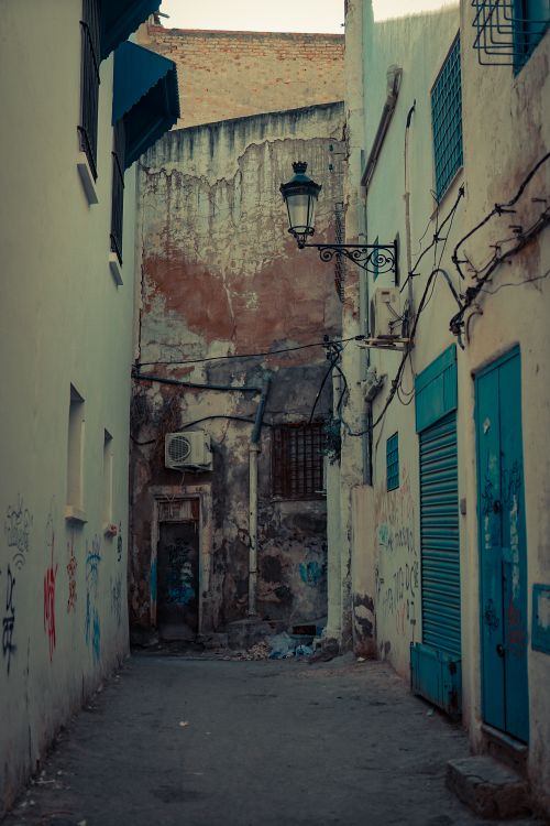 Free A serene view of an old, narrow alleyway with rustic buildings and vintage street lamps. Stock Photo