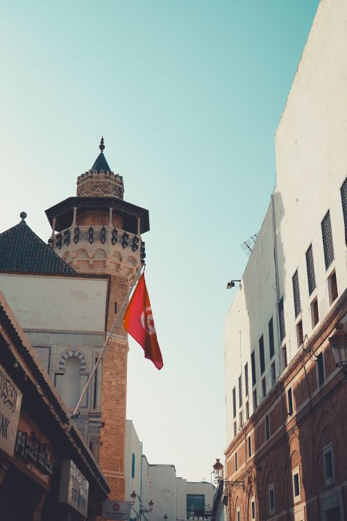 Free A scenic view of a historic medina with a Tunisian flag fluttering near a traditional minaret. Stock Photo