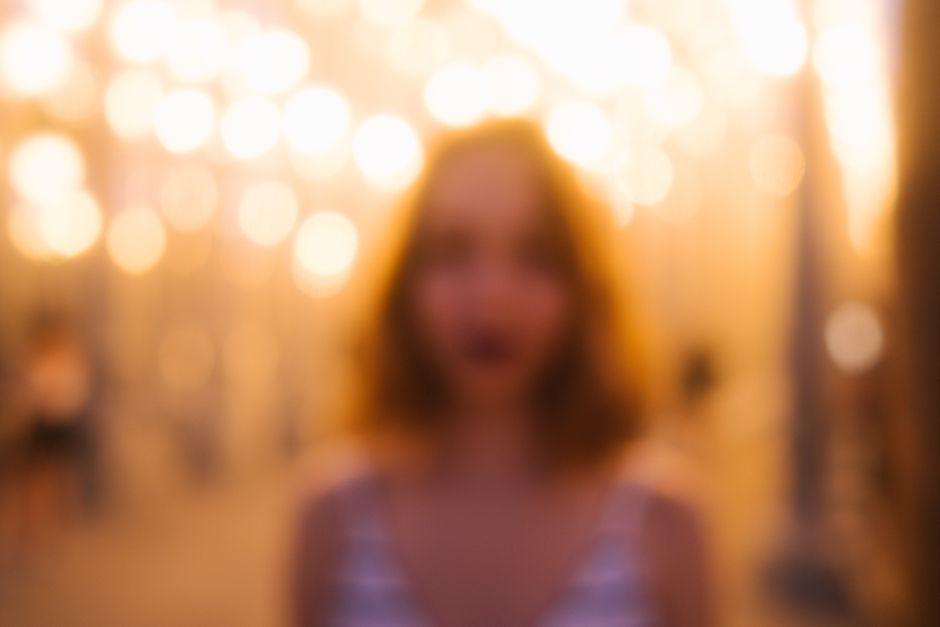Blurred female standing in bright bokeh lights of street illuminated at night time
