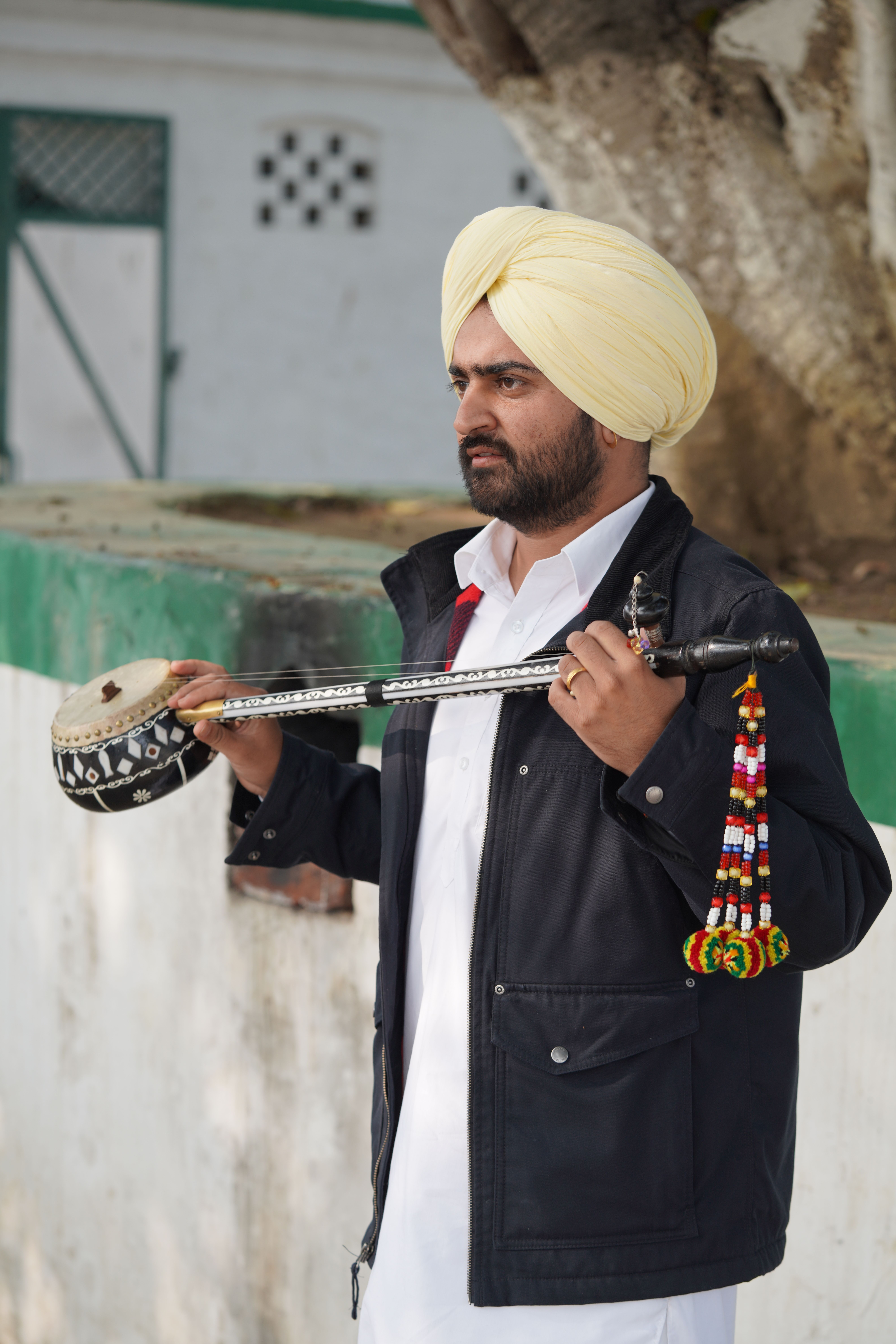 Indian man in turban playing tumbi outdoors, showcasing rich cultural heritage.