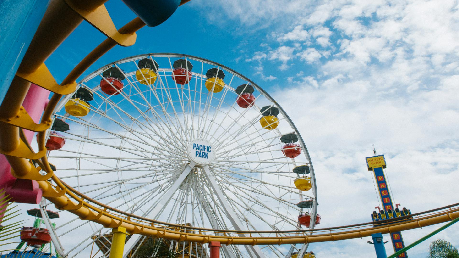 Colorful ferris wheel and roller coaster at Pacific Park with blue sky backdrop.
