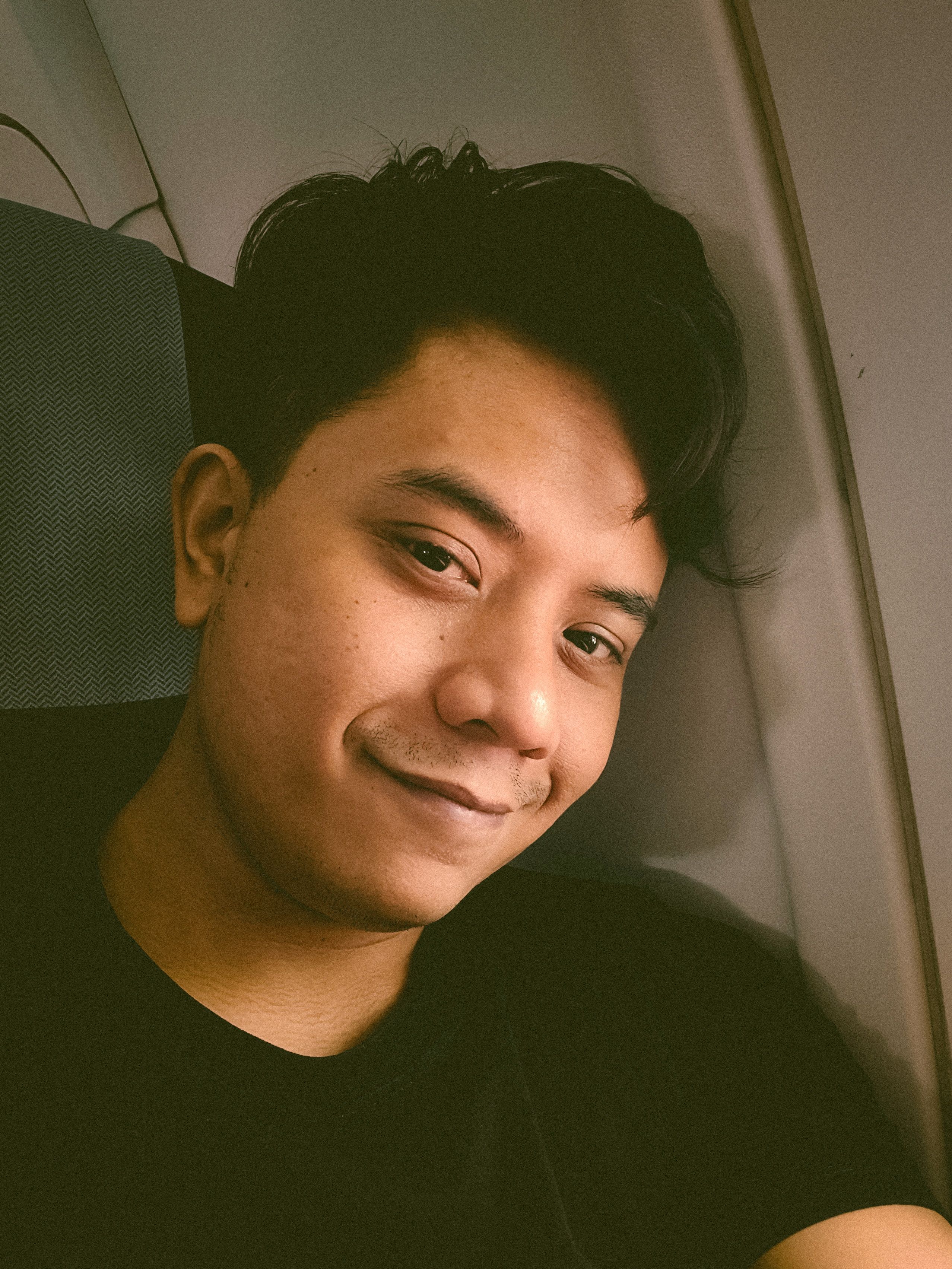 Casual portrait of a young man sitting by an airplane window during a daytime flight.