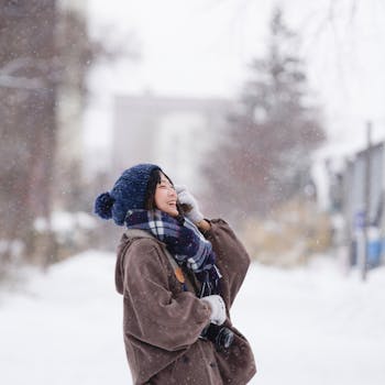 A cheerful woman in winter attire enjoys the snowfall in a serene outdoor setting.