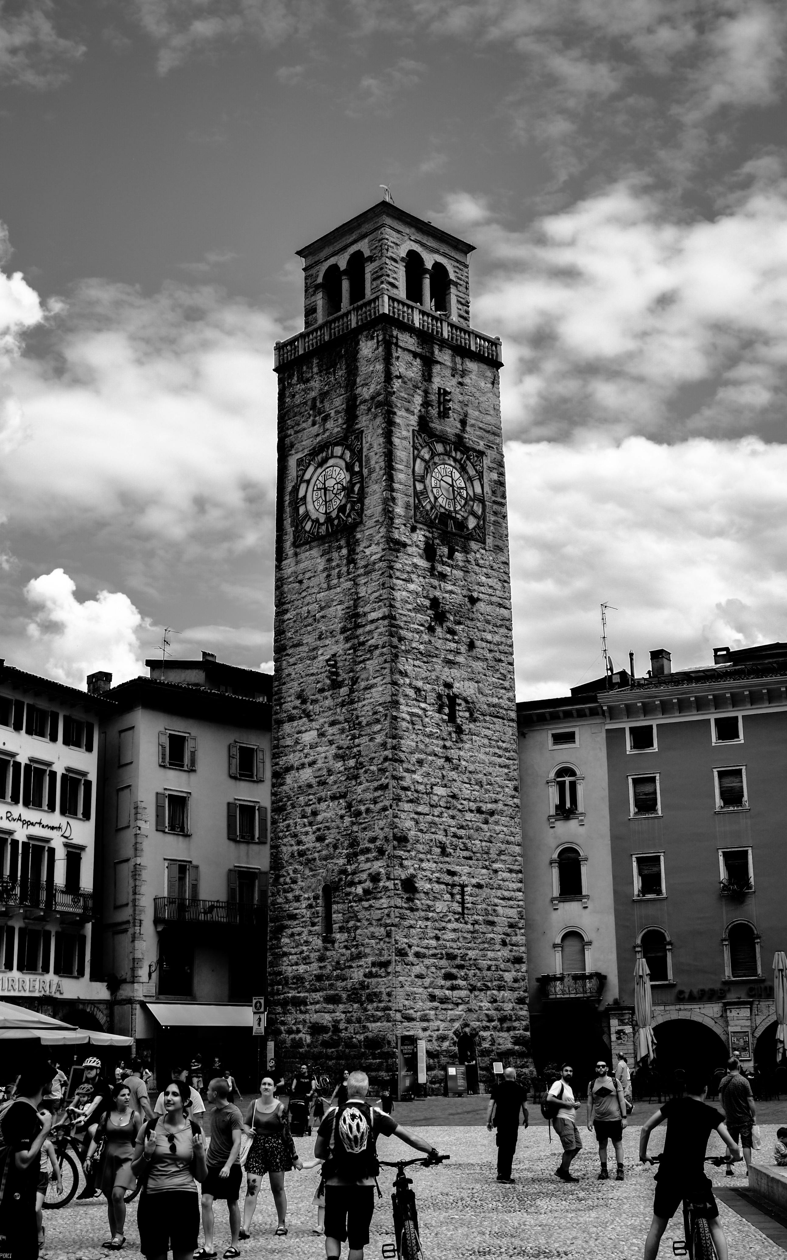 Black and white photo of a historic clock tower in a busy European city square, vibrant street life.