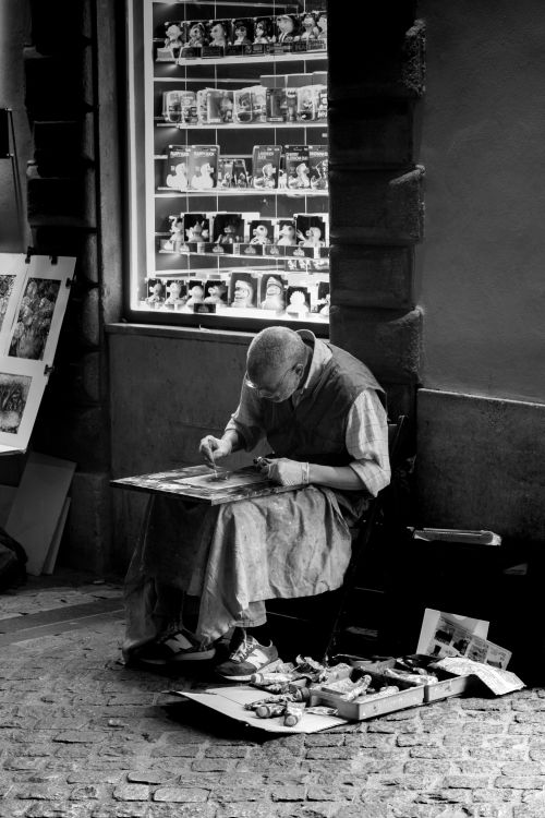Free A street artist sketching outside a shop window displaying figurines. Moody black and white. Stock Photo