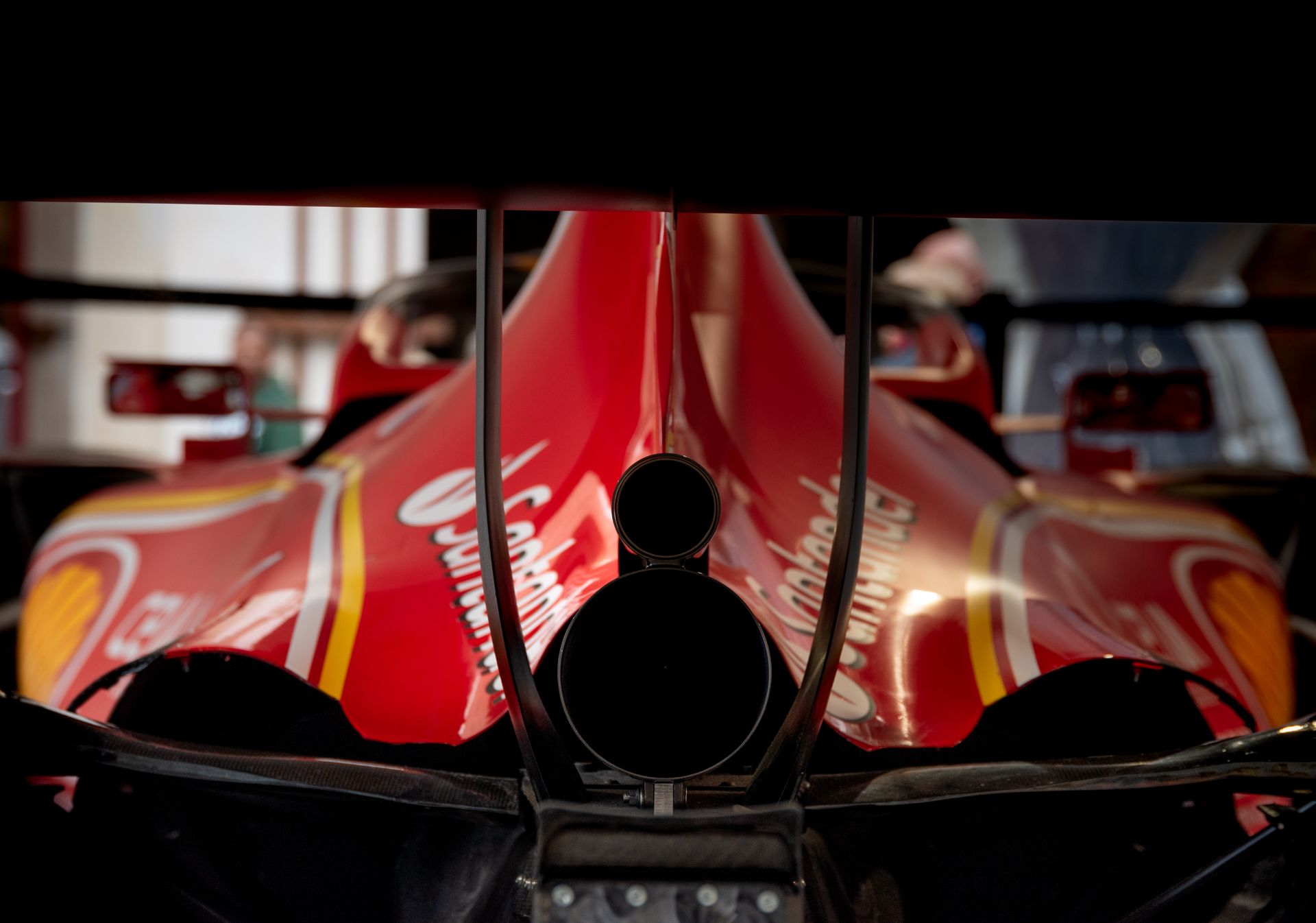 Detailed view of red formula race car's rear with exhaust and logos, indoors.