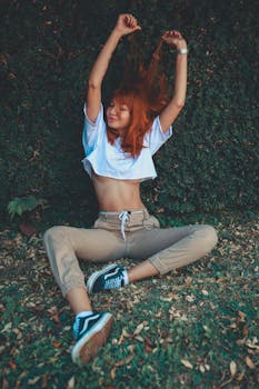 红发女人坐在户外，举起双臂享受夏日