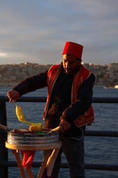 Vendor in cultural attire serves Turkish ice cream by the Bosphorus at sunset.