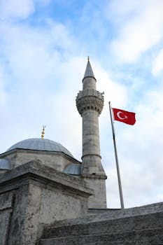 A stunning view of a mosque minaret and Turkish flag against a cloudy sky in Istanbul, Turkey.