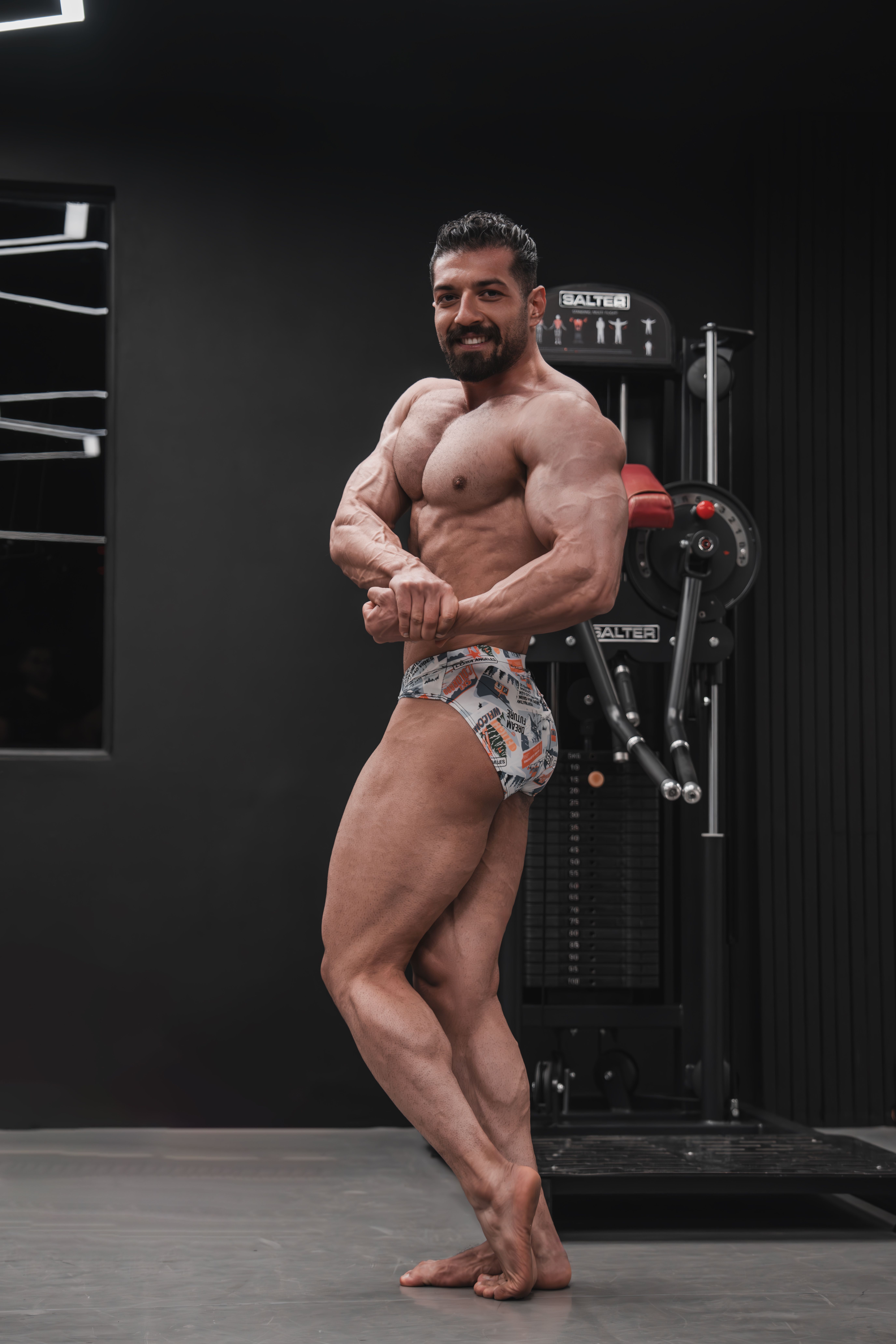 A muscular male bodybuilder showcases his physique indoors at a gym.