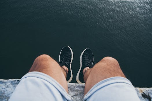 Person sitting on a ledge, looking down at the water below, with legs in view.