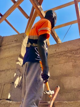 A construction worker building a roof with wooden beams, hammer in hand.
