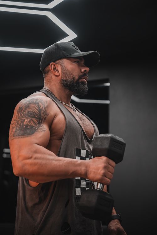 Free Strong man with tattoos lifting dumbbell in modern gym, showcasing fitness and strength. Stock Photo