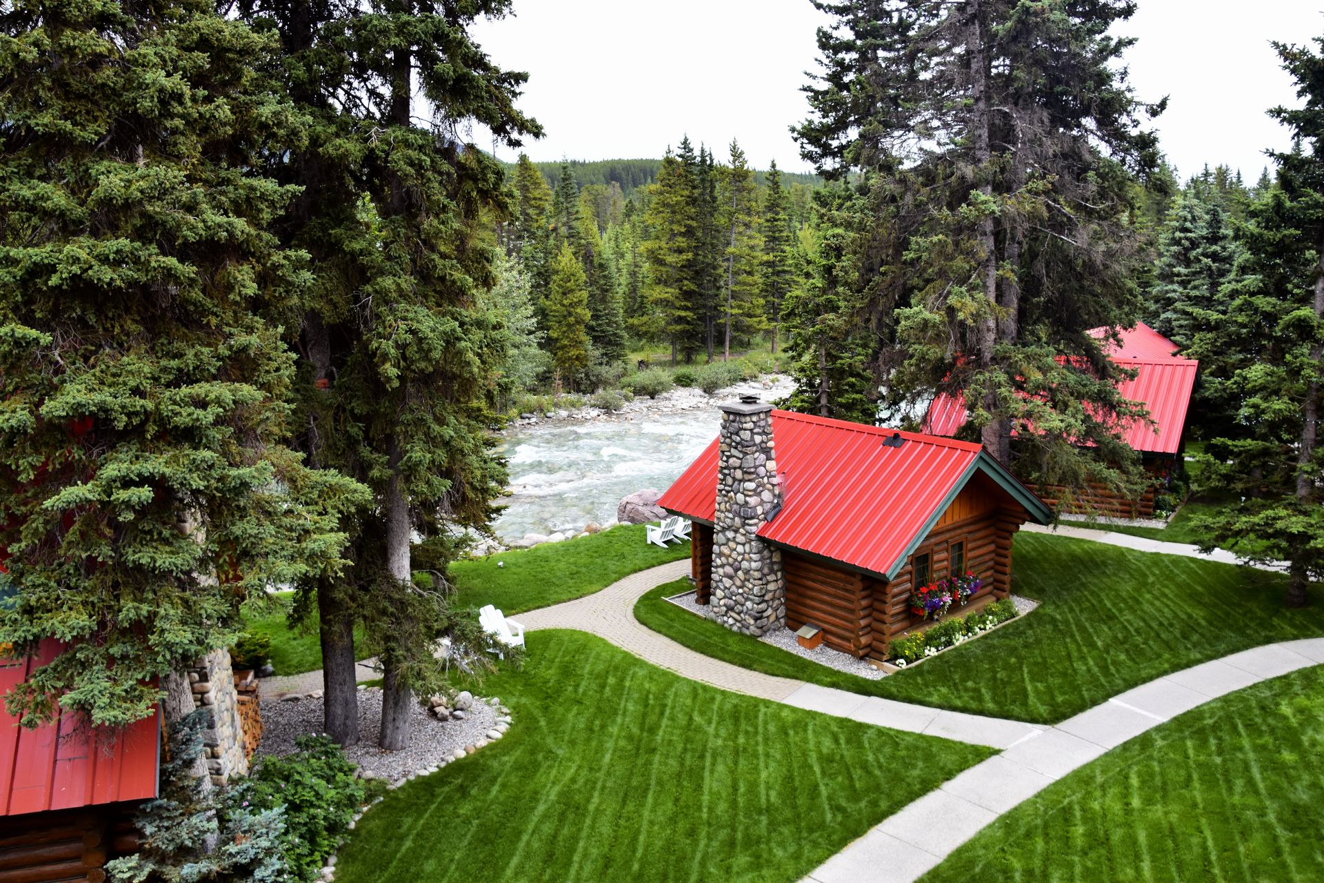 Picturesque log cabins with red roofs surrounded by lush forest and river.