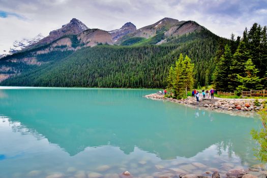 Vibrant lake with stunning mountain backdrop and tourists enjoying the treelined shore.