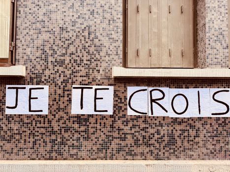 Outdoor mosaic wall featuring the handwritten phrase 'Je Te Crois' in French.