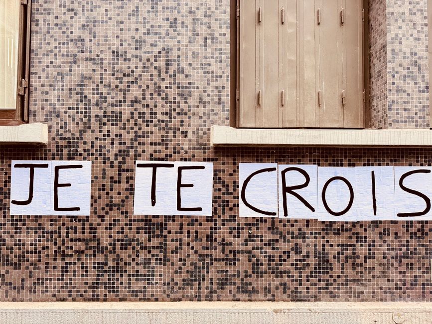 Outdoor mosaic wall featuring the handwritten phrase 'Je Te Crois' in French.