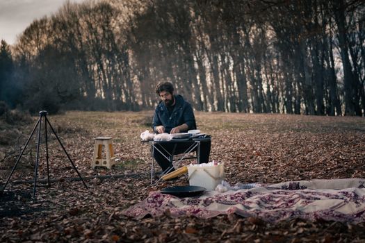 A man enjoys a serene camping experience in a forest during autumn, surrounded by nature.