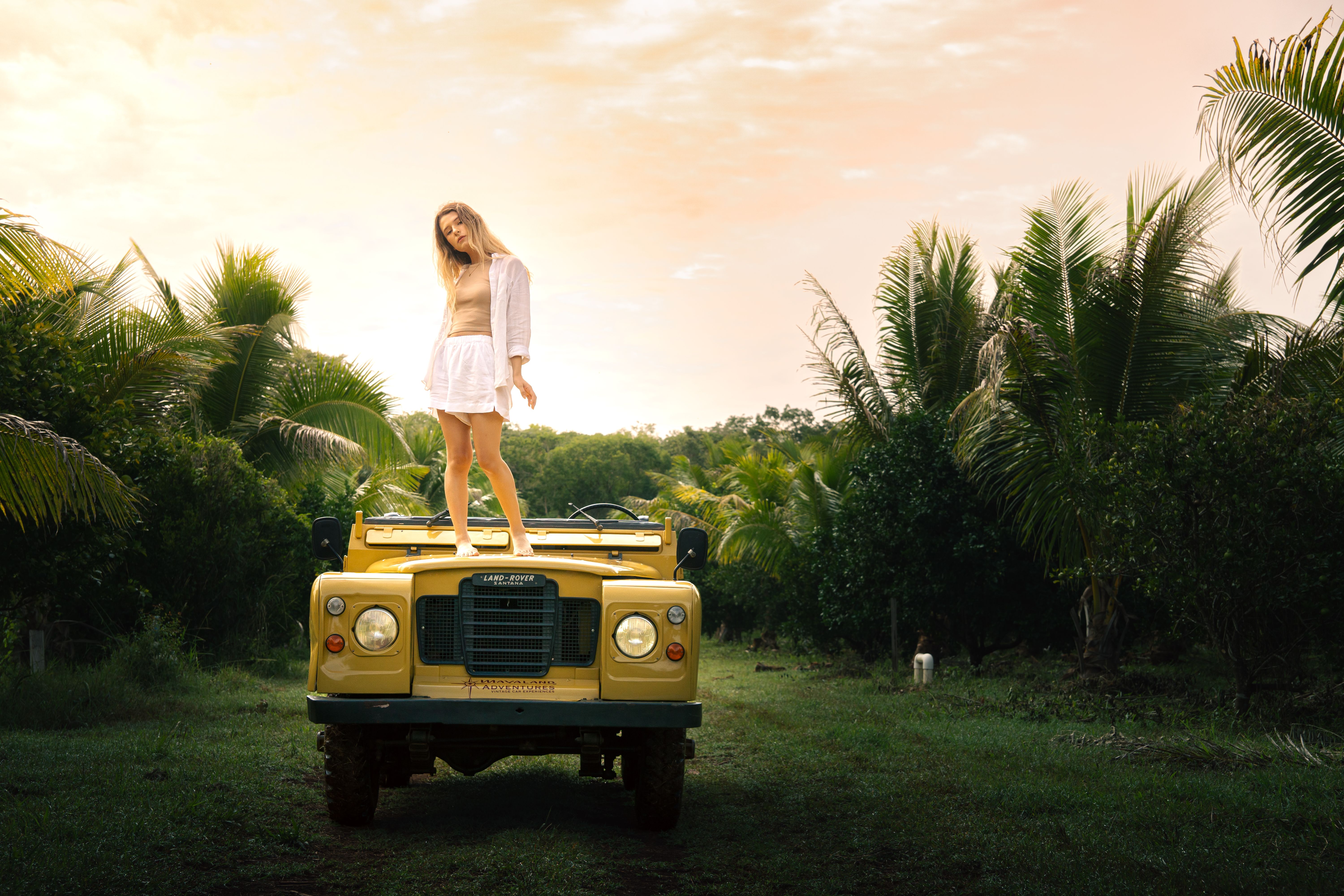 Woman Posing on Land Rover at Sunset in Tropical Setting · Free Stock Photo