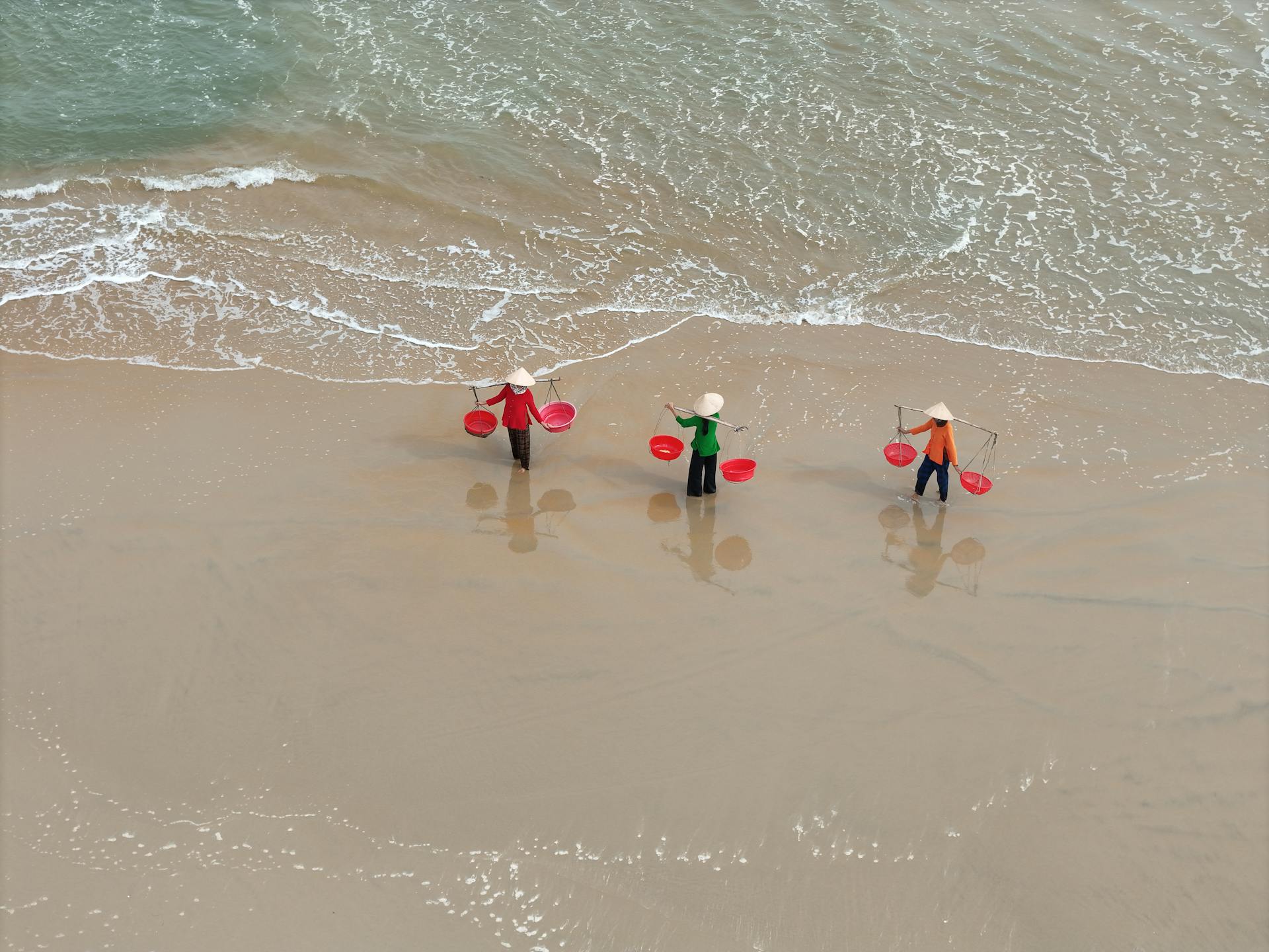 Aerial view of Vietnamese fishermen with conical hats on Hoi An beach, Vietnam.