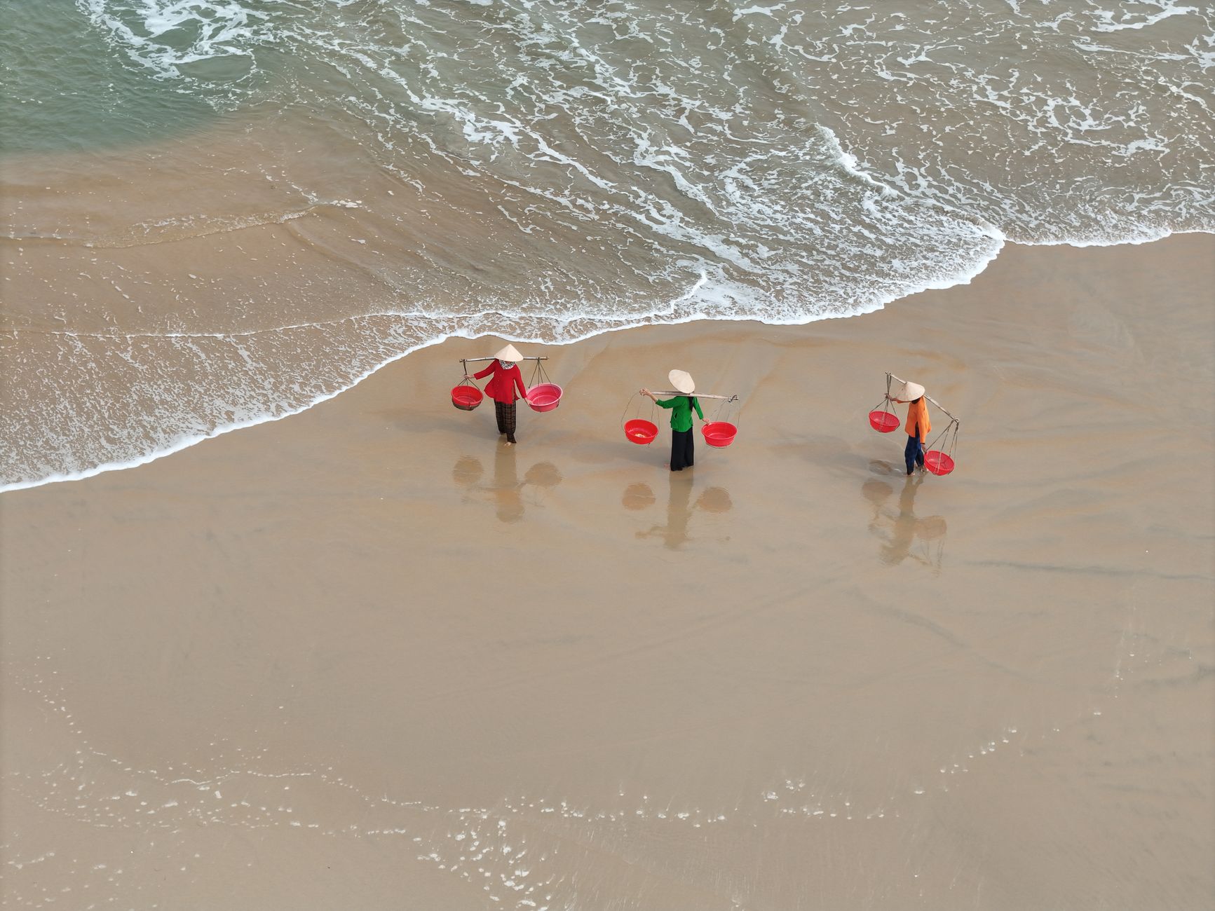Aerial view of Vietnamese fishermen with conical hats walking on a sandy beach.