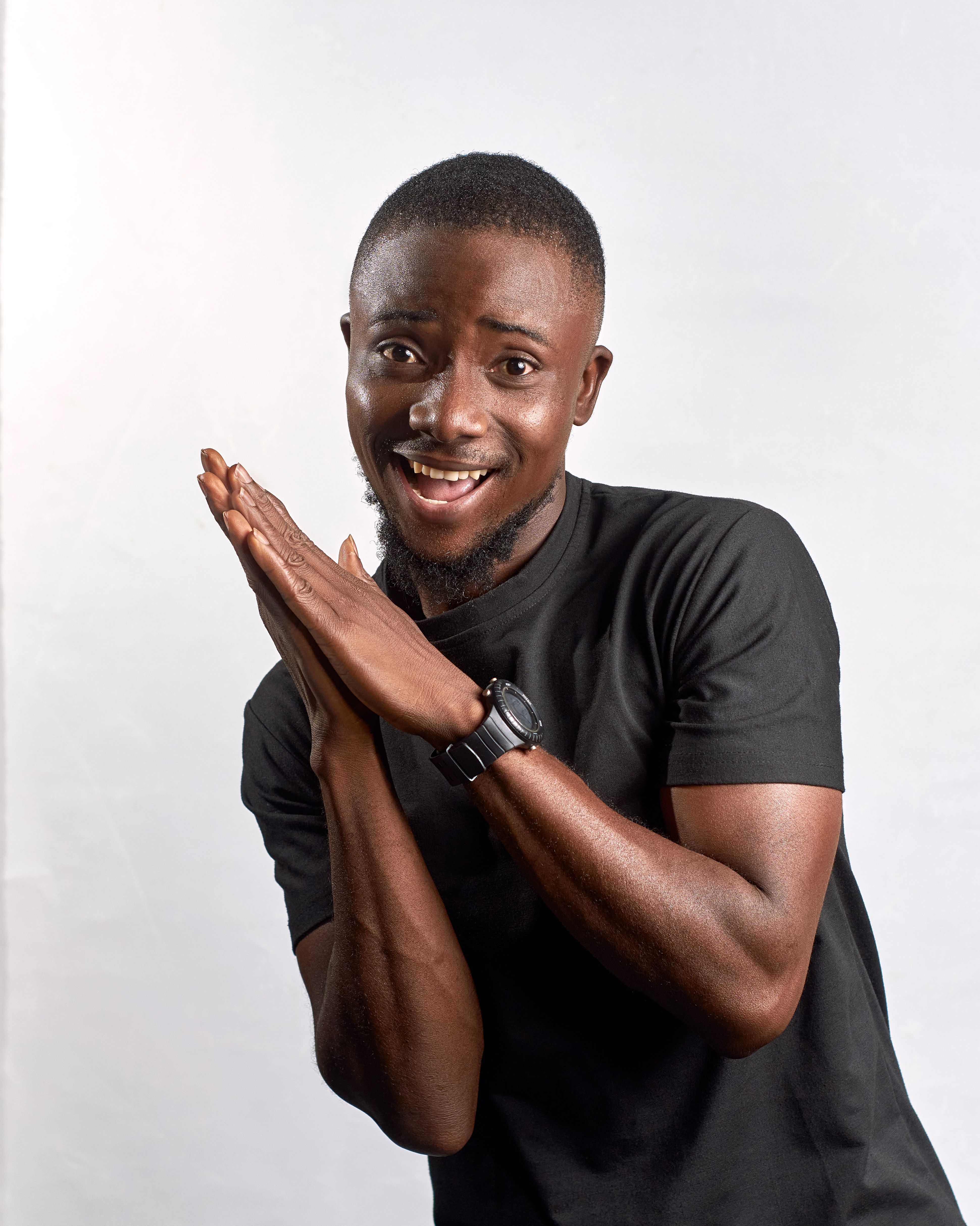 A cheerful African man in a casual pose against a plain background indoors, expressing happiness.