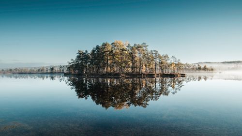 Free Serene sunrise over a tranquil lake with mist and reflection of trees, emphasizing natural beauty. Stock Photo