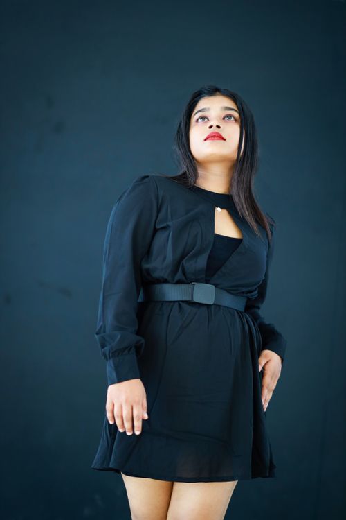 Free Elegant portrait of a woman in a stylish black dress posing confidently against a dark background. Stock Photo