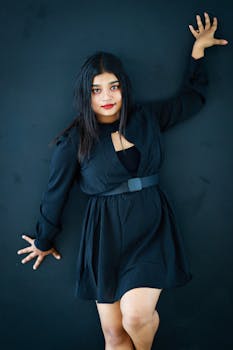 Confident woman poses in elegant black dress, creating a dramatic fashion portrait.