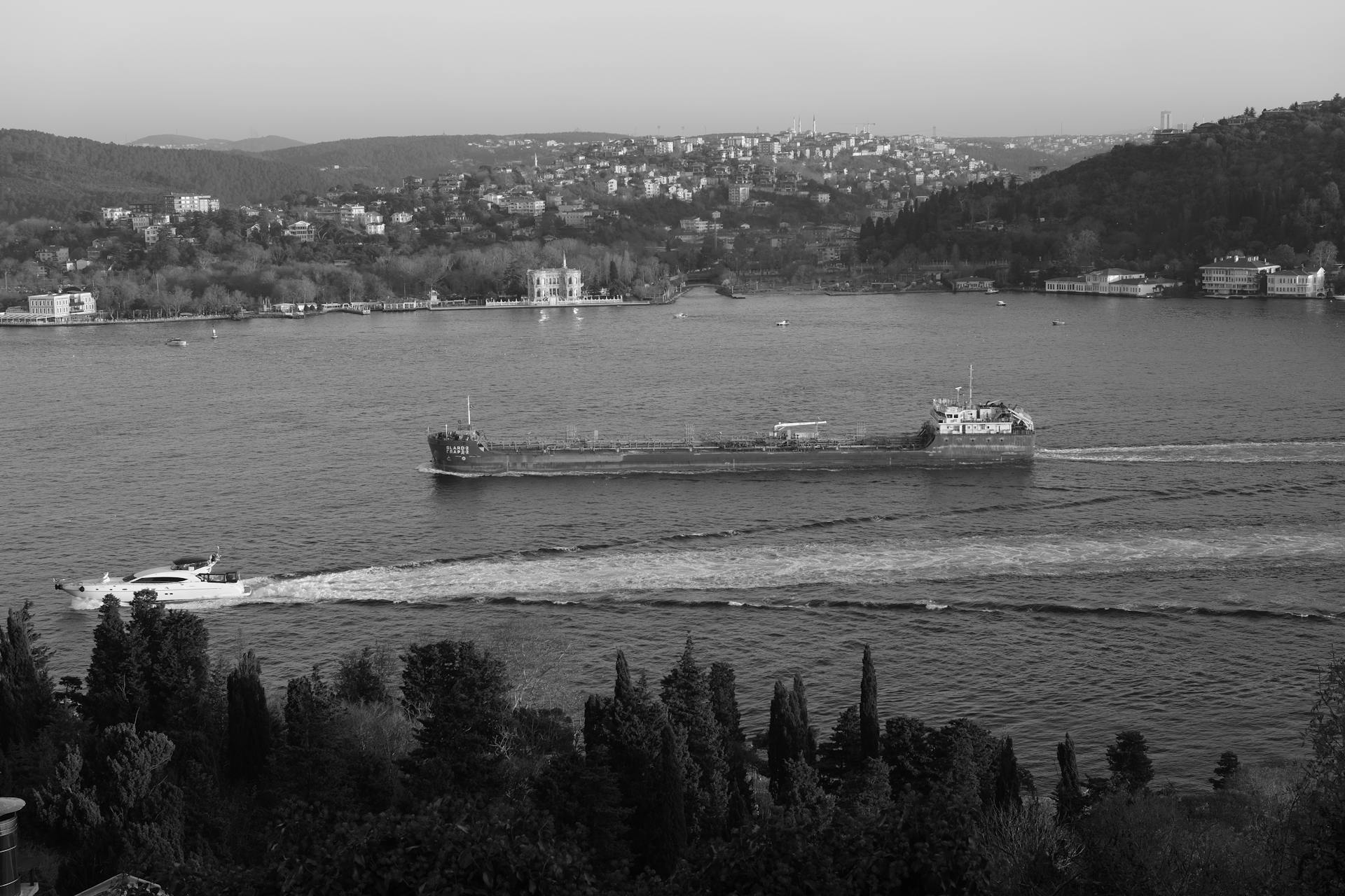 A black and white image captures a cargo ship navigating the Bosphorus Strait in Istanbul on a tranquil day.