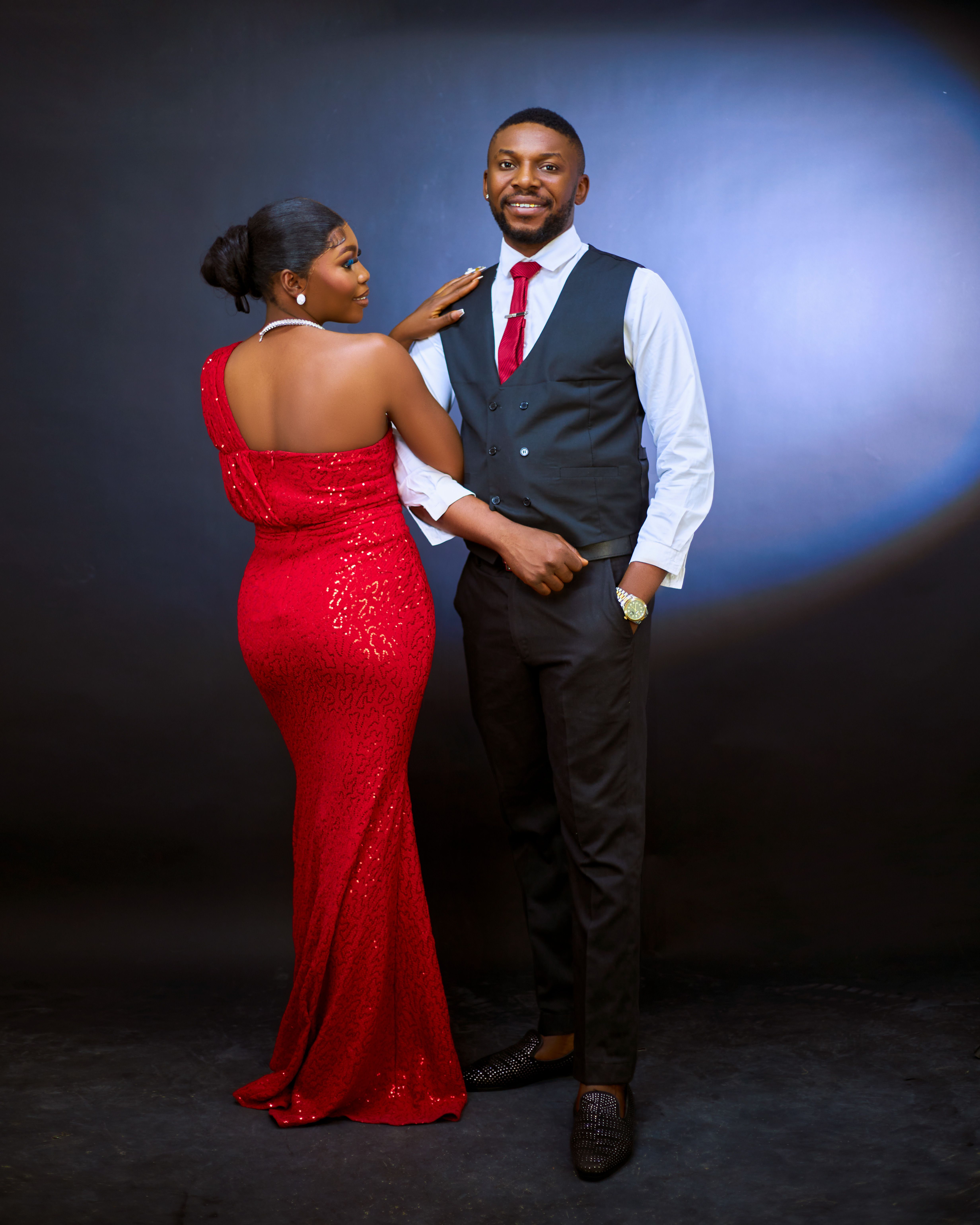 Stylish couple dressed in formal attire posing against a black backdrop. Perfect for fashion or event photography.