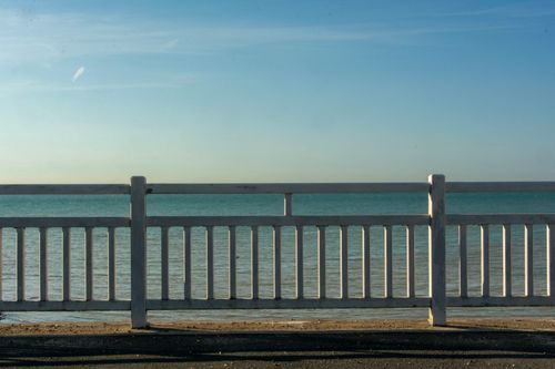 Free Peaceful seascape with a clear sky, viewed through a white wooden fence on a calm day. Stock Photo