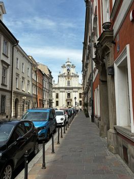 Charming European street lined with parked cars, leading to a majestic historic church under a clear sky.