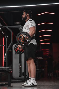 Athletic man performs bicep curls with a barbell in a contemporary gym setting.