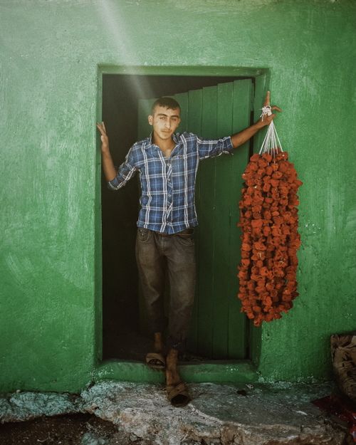 Free A young man stands in a green doorway holding a bunch of dried red peppers. Stock Photo