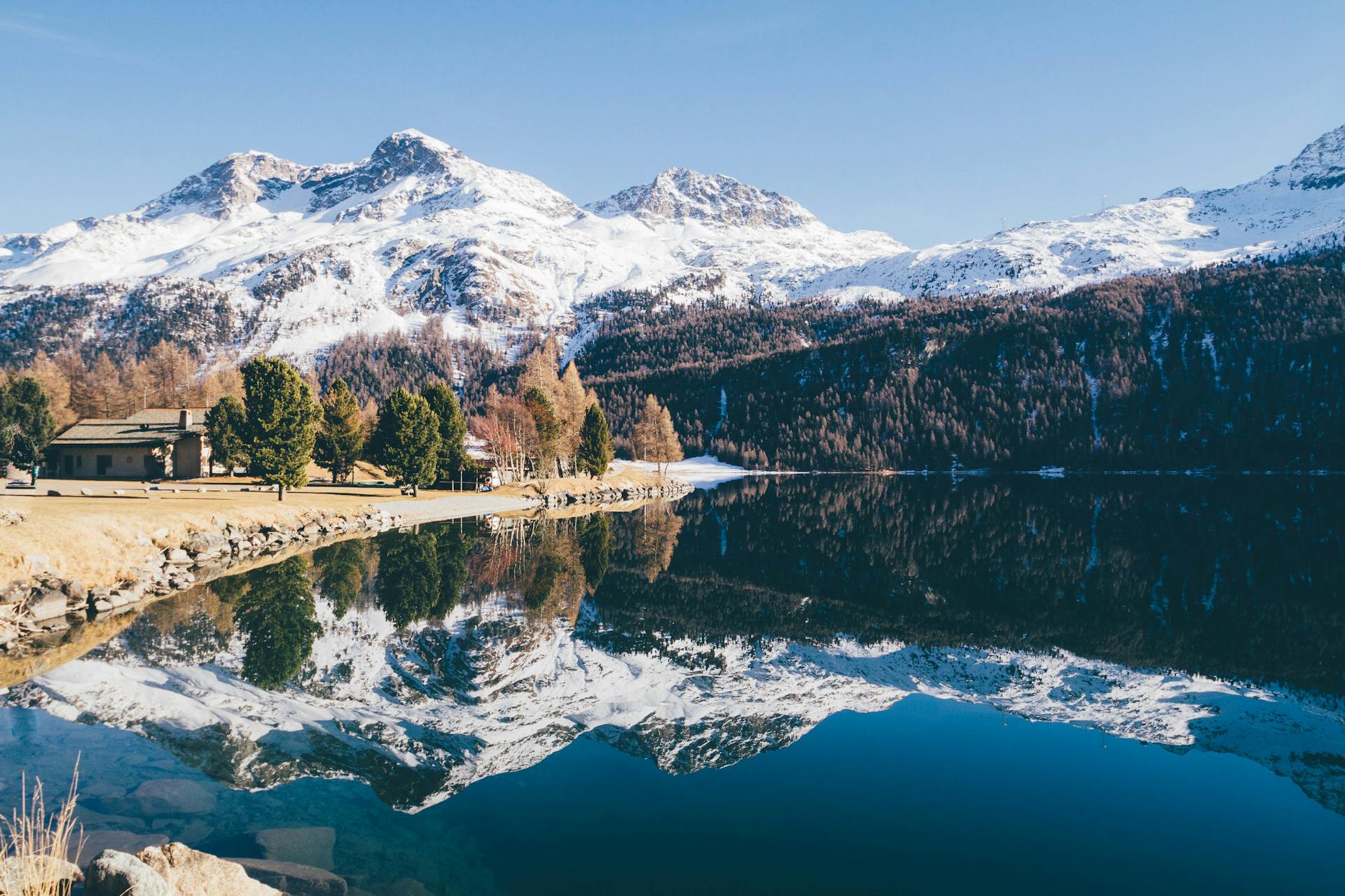 Peaceful lake with snow-capped Swiss Alps reflecting on a clear winter day.