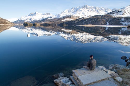 Kostenlos Mann Sitzt Am Rande Des Felsens Mit Blick Auf Den See Während Des Tages Stock-Foto