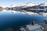 平静的湖面倒映着雪山的宁静景色，岸边坐着一位孤独的人
