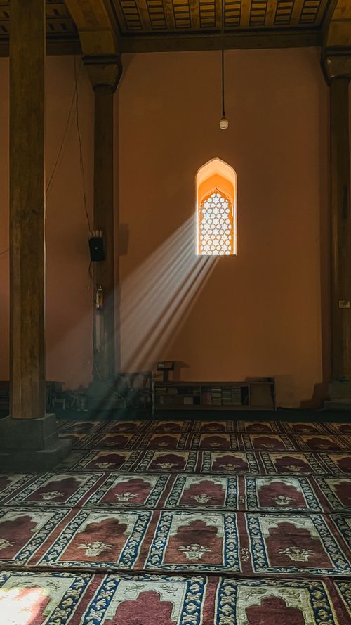 Free Beautiful mosque interior with sunlight streaming through window, illuminating patterned carpets. Stock Photo