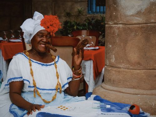 Free Cheerful woman in traditional attire with cigar at outdoor cafe. Vibrant and cultural. Stock Photo