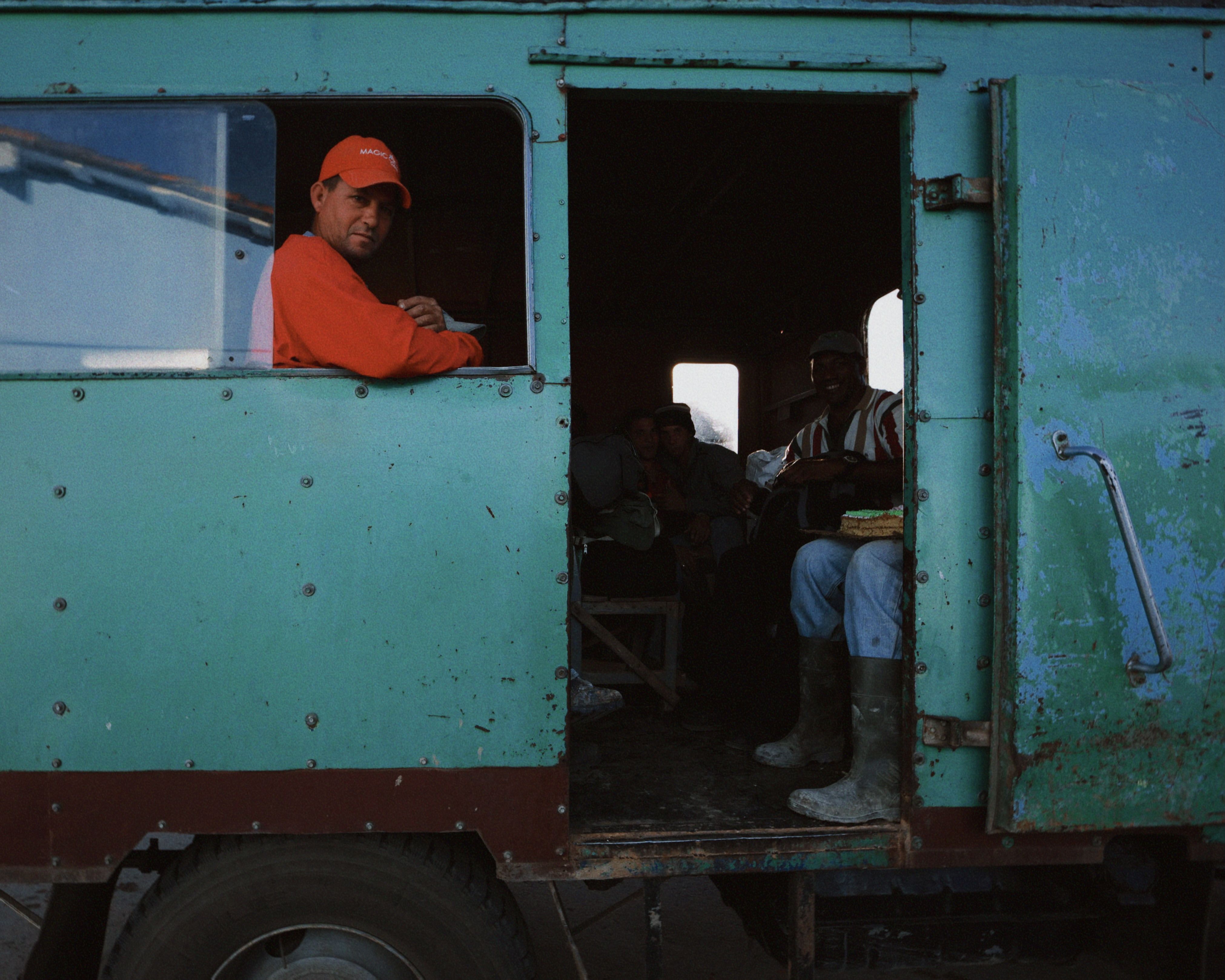 Group of men seated inside a rustic vintage truck van during the day.
