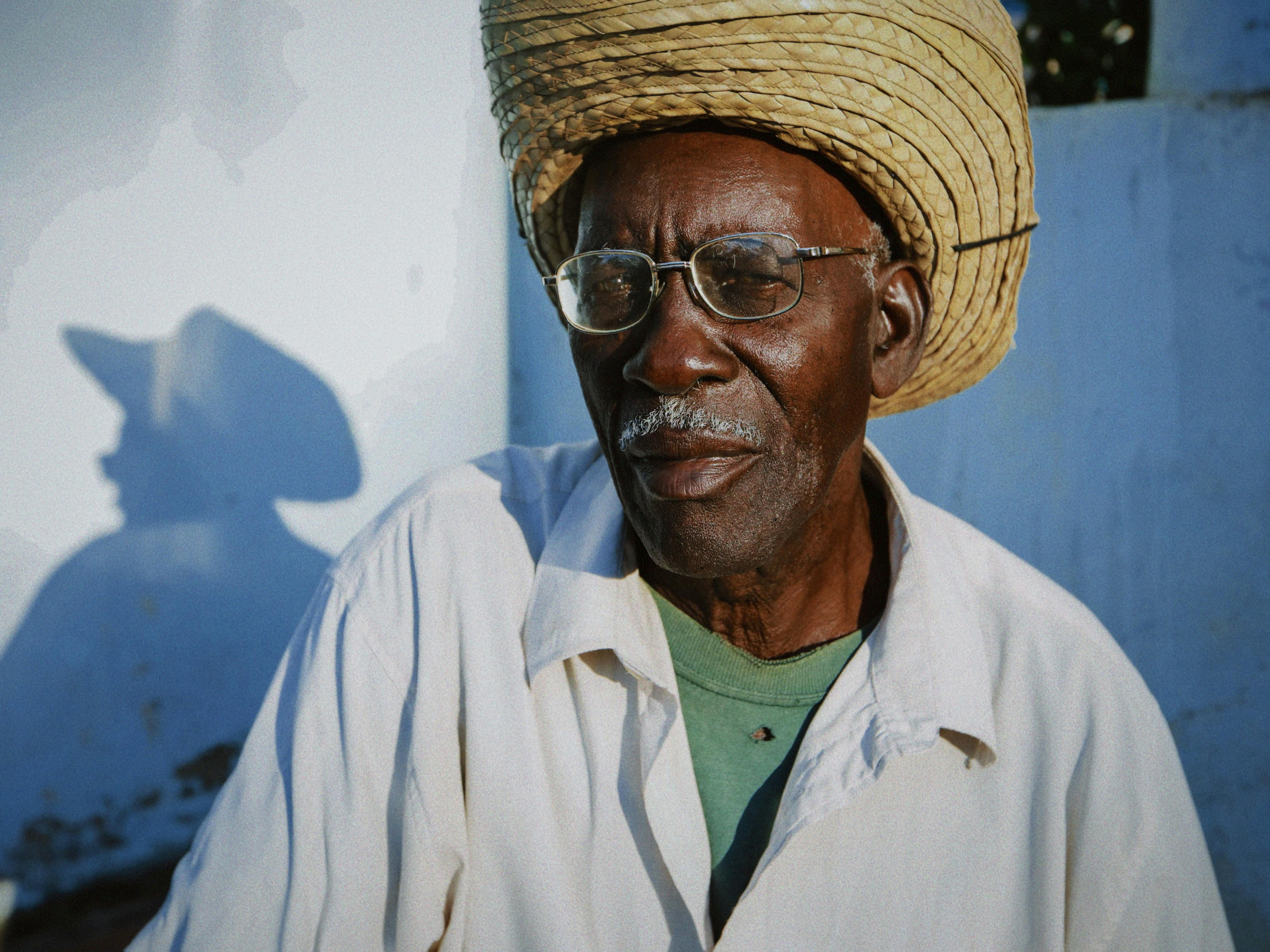 Gratis Portrett av en eldre mann iført en stråhatt mot en solrik vegg, og kaster en skygge. Arkivbilde
