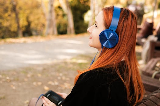 Young woman with red hair enjoying music outdoors with blue headphones during fall.