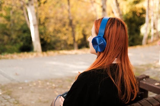 A woman sitting on a bench with blue headphones, enjoying the autumn scenery.