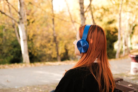 Red-haired woman with blue headphones relaxing in a park during autumn.
