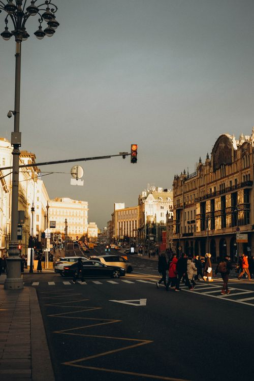 Free Urban street scene with pedestrians crossing and cars driving by under warm evening light. Stock Photo