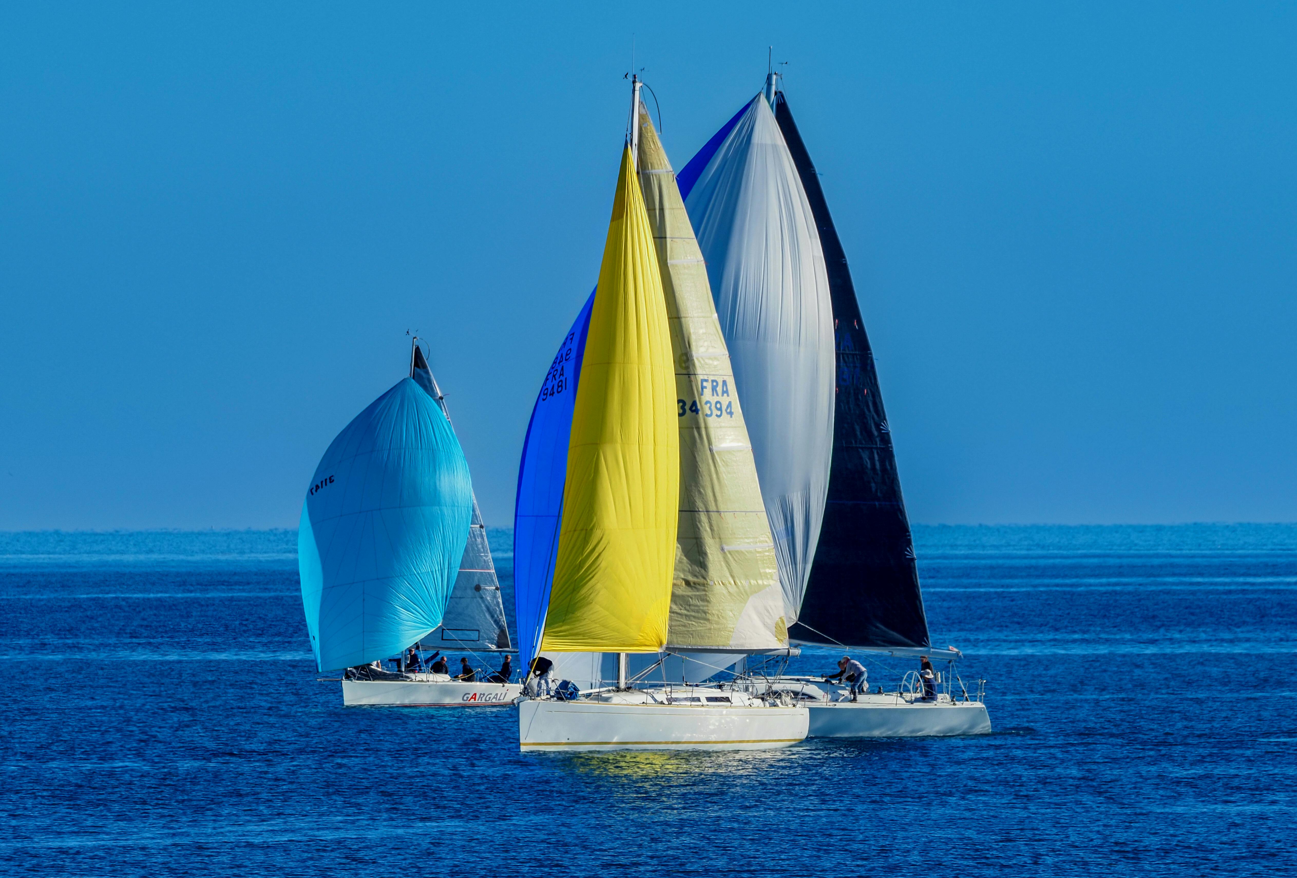 Three vibrant sailboats competing in a sailing race on the open sea under a clear blue sky.